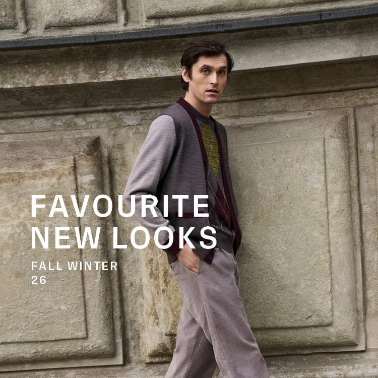ENGLISH FORMALITY Men: Mann in Strickjacke mit Kontrastdetails über Strickpullover und Tailoring Hose vor historischer Architektur.