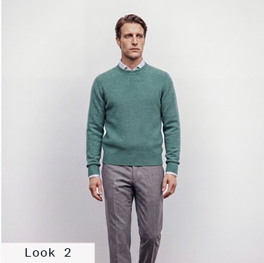 Look 2 English Formality Men: Mann im grünen Feinstrickpullover über hellem Hemd mit grauer Stoffhose vor hellem Hintergrund.