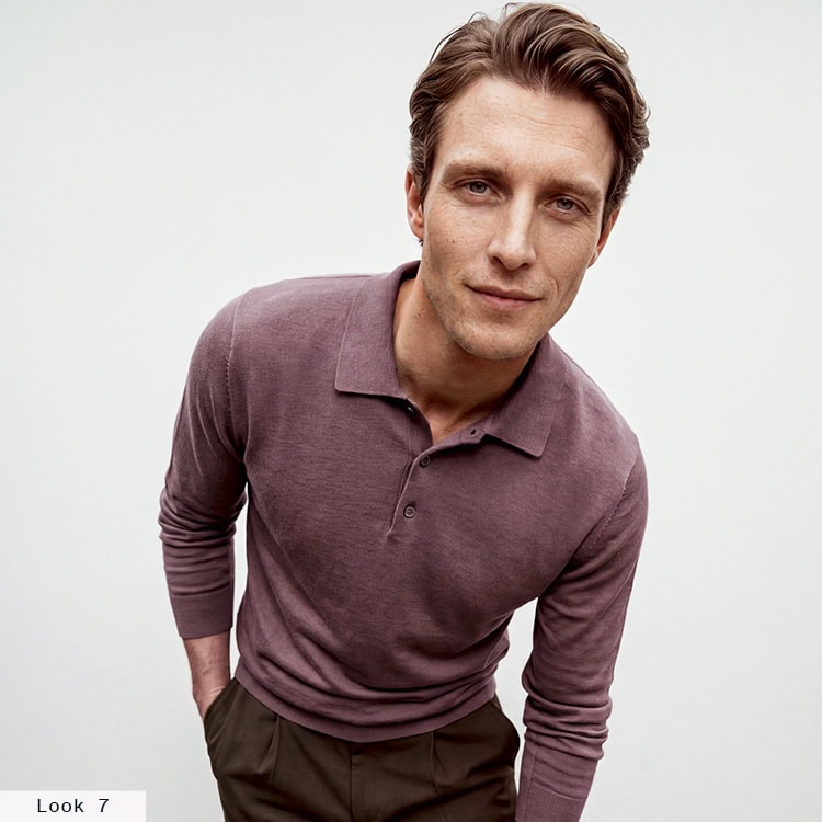 Look 7 English Formality Men: Mann im mauvefarbenen Feinstrickpolo mit dunkler Stoffhose vor hellem Hintergrund.