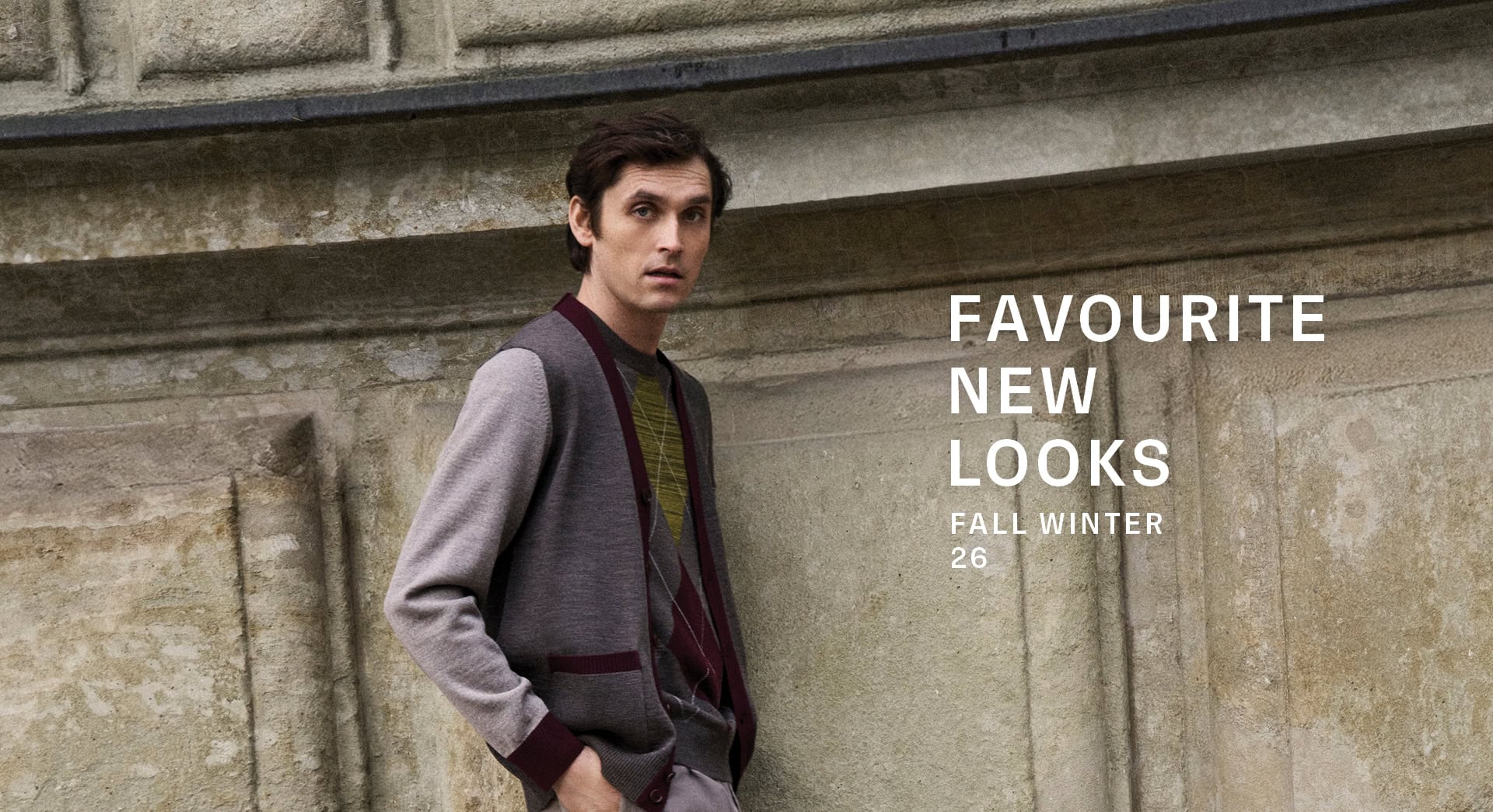 ENGLISH FORMALITY Men: Mann in Strickjacke mit Kontrastdetails über Strickpullover und Tailoring Hose vor historischer Architektur.