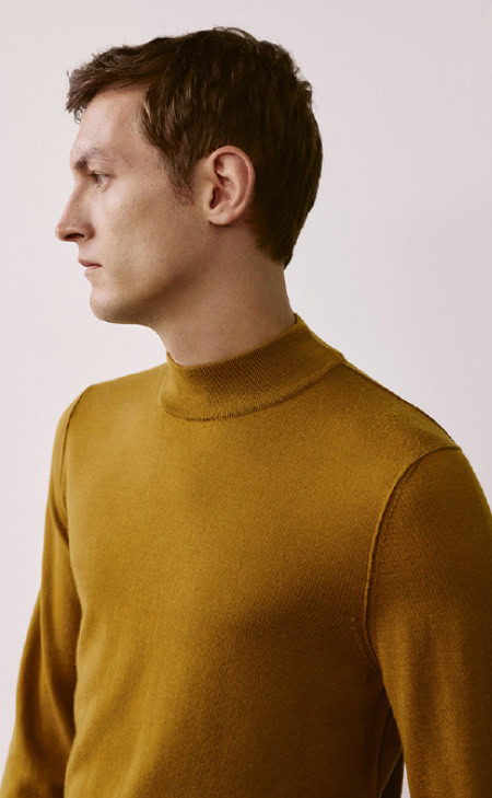MAERZ Muenchen – Merino Classics Mann trägt gelben Strickpullover mit feiner Struktur und Stehkragen vor neutralem Hintergrund.