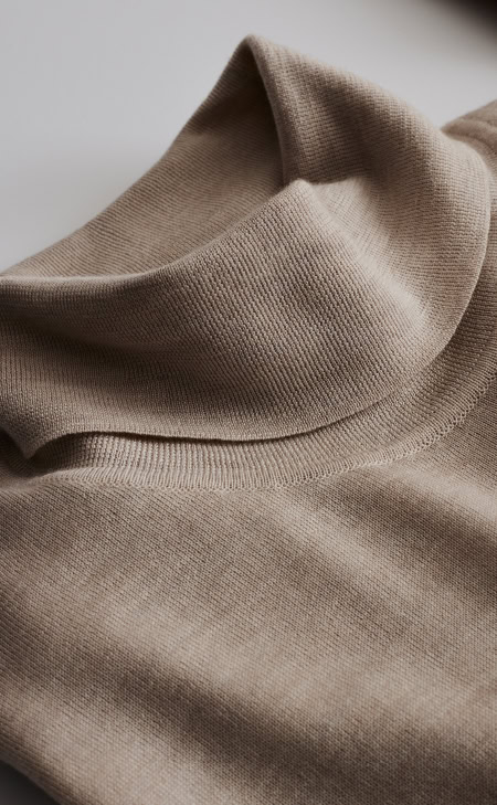 Detailansicht eines beigen Merino-Rollkragenpullovers mit feiner Strickstruktur.