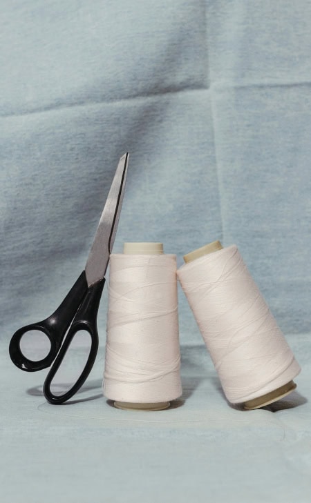 MAERZ Muenchen – Linen Zwei Garnspulen in hellem Beige und schwarze Schneiderschere auf hellblauem Stoffhintergrund.