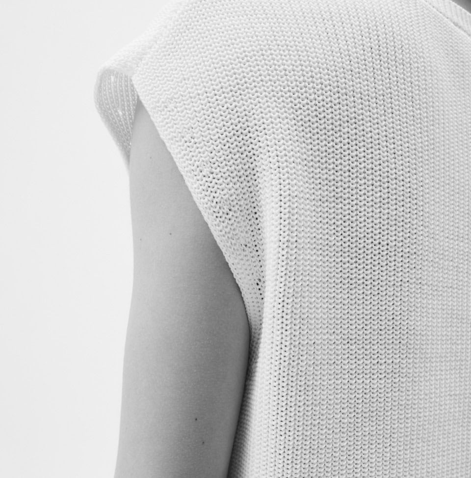 Nahaufnahme eines weißen Stricktops aus Baumwolle, Fokus auf feine Maschenstruktur und hochwertige Verarbeitung.