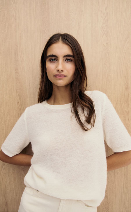 Frau in weichem Alpaka‑Wollpullover, modern und natürlich vor hellem Holz inszeniert – luxuriöse Alpaka‑Faser für hochwertige Premium‑Knitwear.