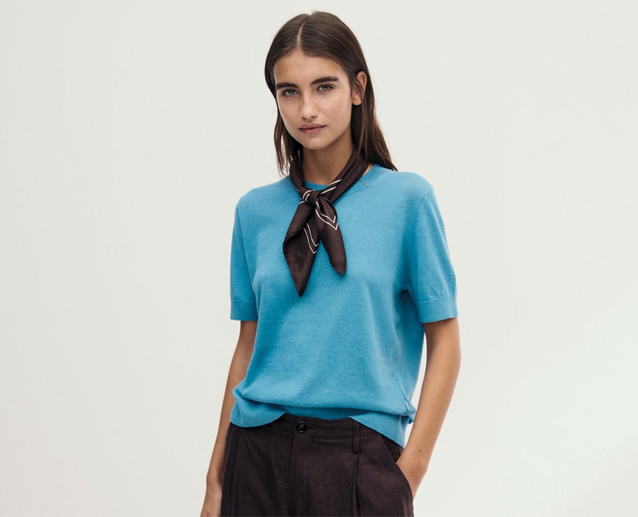 Frau in leichtem Cotton‑und‑Linen T-Shirt, modern und klar im Studio inszeniert – natürliche Sommermaterialien für hochwertige Premium‑Looks.