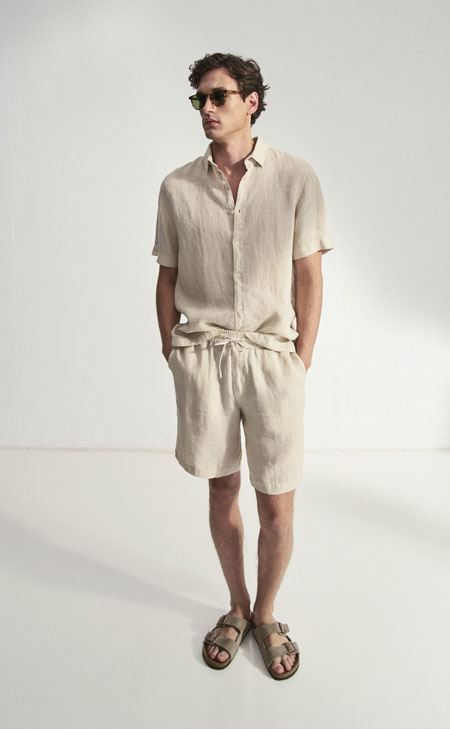 Mann in hellem Leinen‑Set aus Kurzarmhemd und Shorts, modern und leicht im Studio inszeniert – luftiges Premium‑Leinen für Sommerlooks.