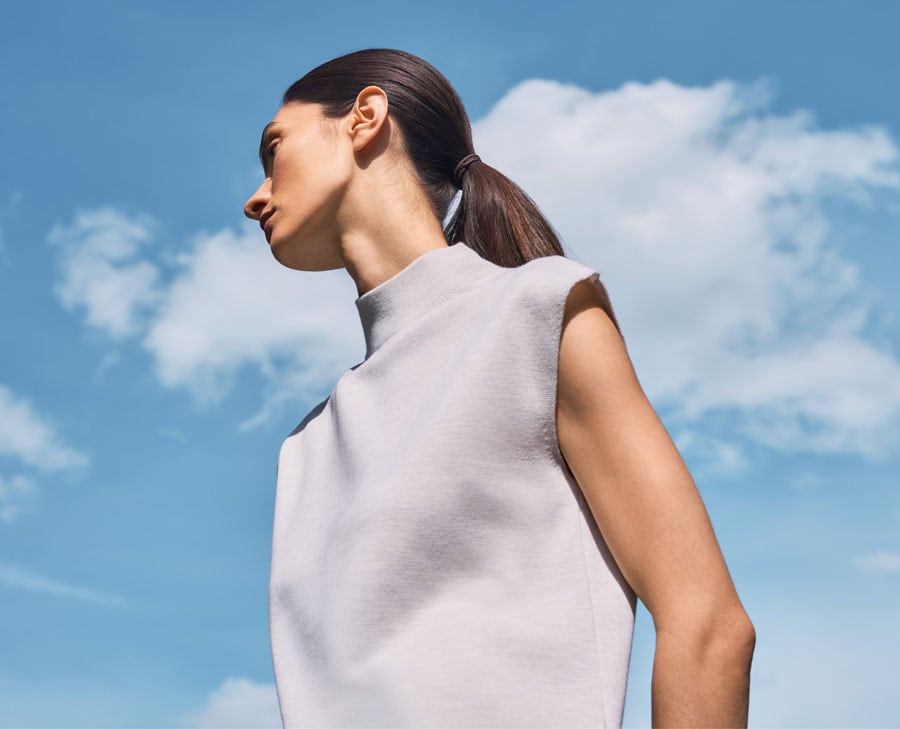 Frau in leichter Merino‑Air Silhouette vor blauem Himmel, modern und luftig inszeniert – extrafeiner Strick für natürliche Premium‑Looks.