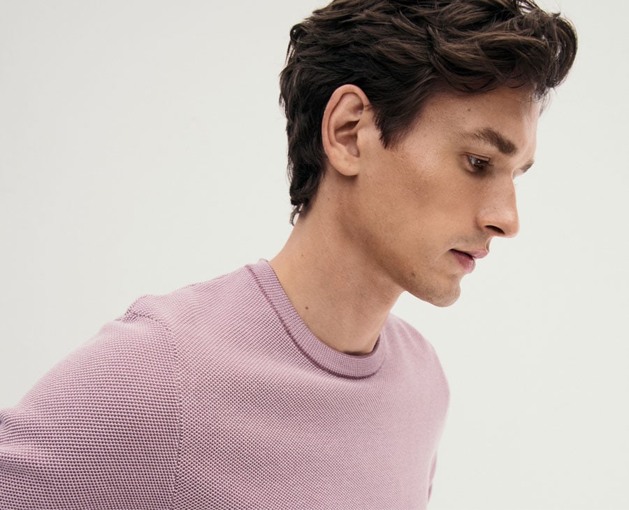 Mann im feinen Strickpullover in zartem Flieder, modern im Studio inszeniert – hochwertige Herren‑Knitwear für zeitlose Premium‑Looks.