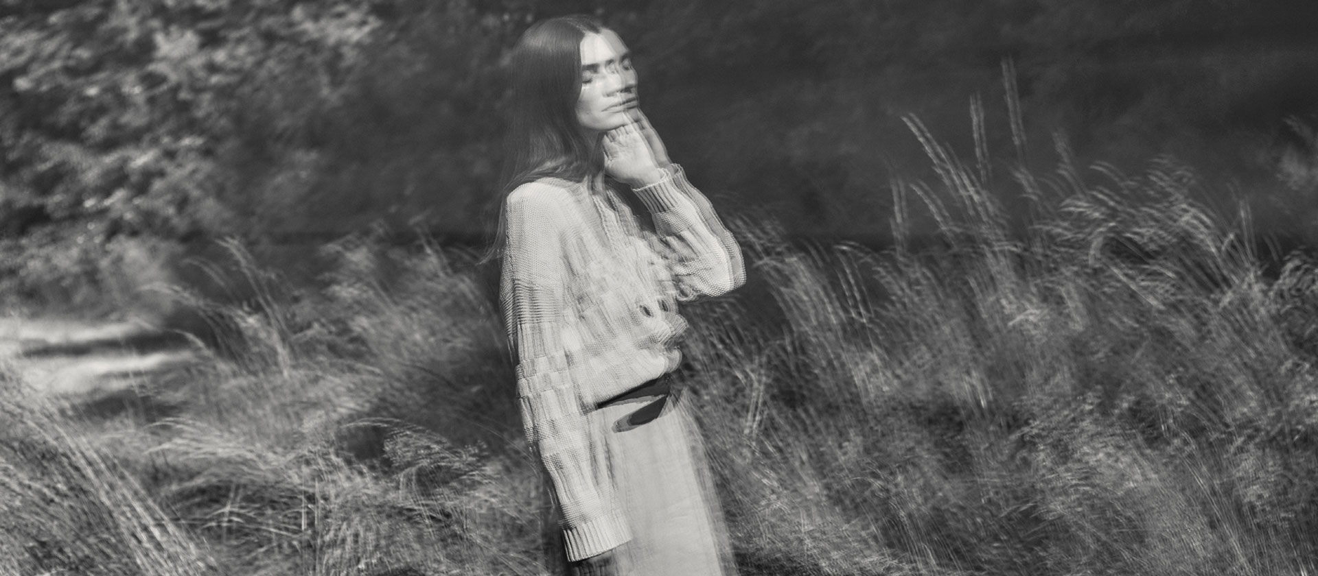 Frau in fließendem Organic‑Cotton Look, sanft und natürlich in der Landschaft inszeniert – moderne Premium‑Ästhetik in reiner Bio‑Baumwolle.