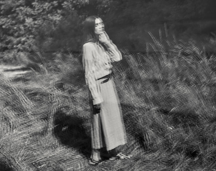 Frau in fließendem Organic‑Cotton Look, sanft und natürlich in der Landschaft inszeniert – moderne Premium‑Ästhetik in reiner Bio‑Baumwolle.